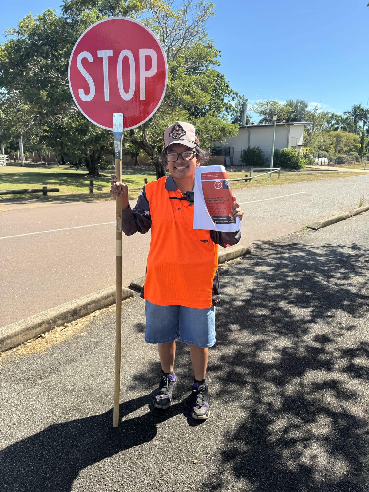 Participant holding a traffic STOP sign on a Darwin street during supported work